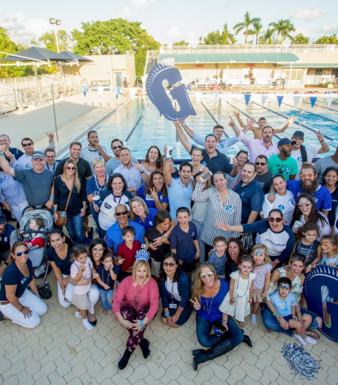 Large alumni group posing by the pool and holding Gulliver signs