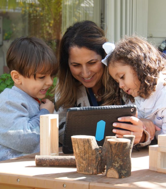 Two kids looking at an ipad with a teacher