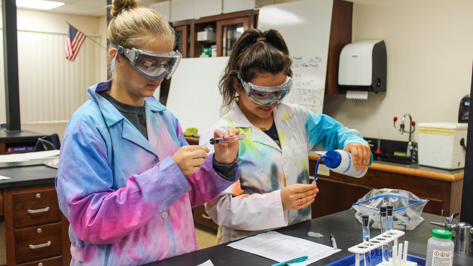 Two girls in chemistry class wearing protective gear