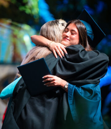 A graduate in a cap and gown embraces another person during a commencement ceremony.