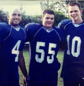 Three football players wearing blue jerseys with the numbers 4, 55, and 10 standing side by side for an alumni spotlight.