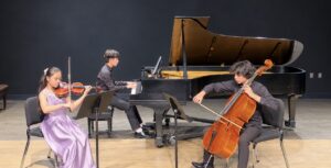 A violinist, a pianist, and a cellist performing on stage.