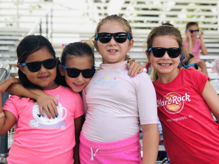 4 girls wearing sunglasses and smiling at camp