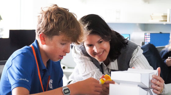 A student and a teacher work together on a white paper architectural model.
