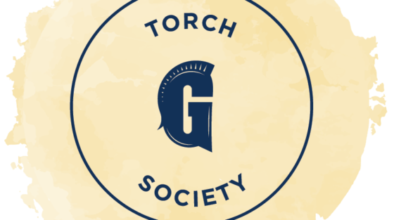 Torch Society logo featuring a dark blue Spartan helmet forming the letter G inside a circle against a pale yellow watercolor background for the alumni spotlight.