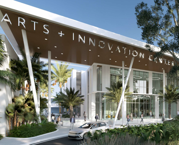 Modern building labeled “Arts + Innovation Center” with glass facade, surrounded by palm trees, landscaped greenery, and people walking near a circular driveway.