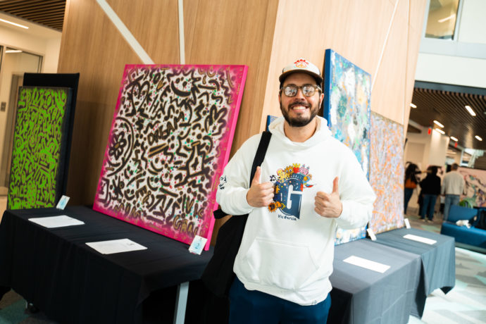 Man giving two thumbs up next to a painting.